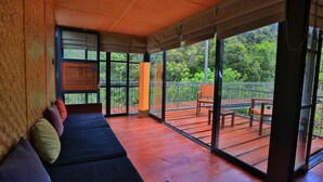 A covered outdoor seating area with a wooden bench and a sofa, large windows, and a view of greenery. - The Rainforest Ecolodge Sinharaja (Deniyaya)