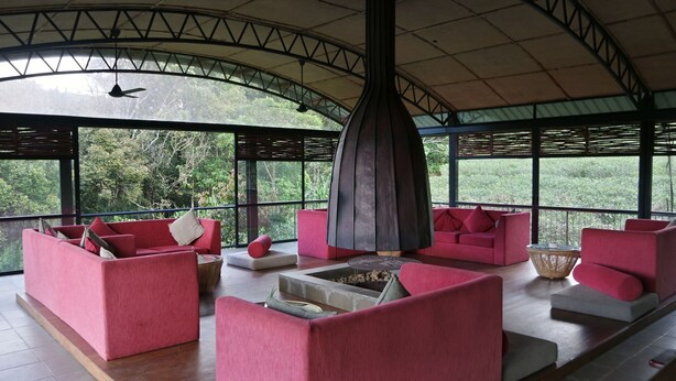 A spacious lounge with red sofas and a central fire pit, large windows offering a view of the surrounding greenery. - The Rainforest Ecolodge Sinharaja (Deniyaya)