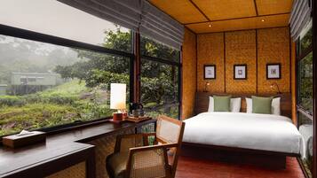 A room with a bed, a desk, and a chair, with a view of greenery outside.
