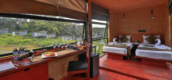 A room with two beds, a desk with a laptop, a telephone, and a view of greenery outside.