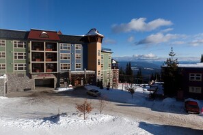 Un hotel de varios pisos con estilo refugio de esquí, un estacionamiento y vistas a montañas nevadas.