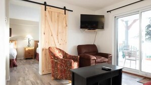 A modern living room with a sliding wooden door, a mounted TV, a brown leather chair, a patterned armchair, and a black coffee table. - Vance Creek Hotel & Conference Centre (Silver Star Mountain)