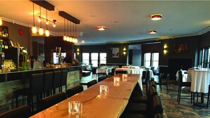 A long wooden bar with a high counter, multiple hanging pendant lights, and a seating area with tables and chairs. - Vance Creek Hotel & Conference Centre (Silver Star Mountain)