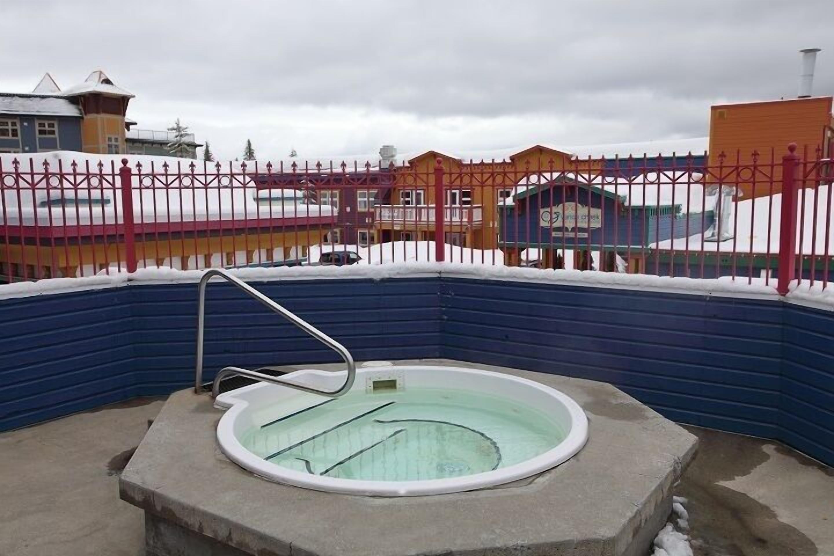 A hot tub surrounded by a snow-covered fence, with buildings in the background.