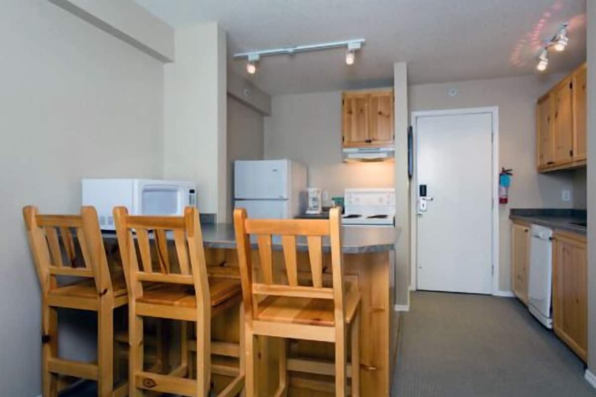 Una cocina compacta con armarios de madera, microondas, refrigerador y un comedor con sillas de madera.