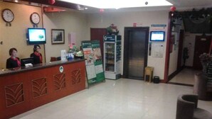 A reception area with a reception desk, two staff members, a clock, a television, and a vending machine. - Green Tree Inn Express (Weihai)