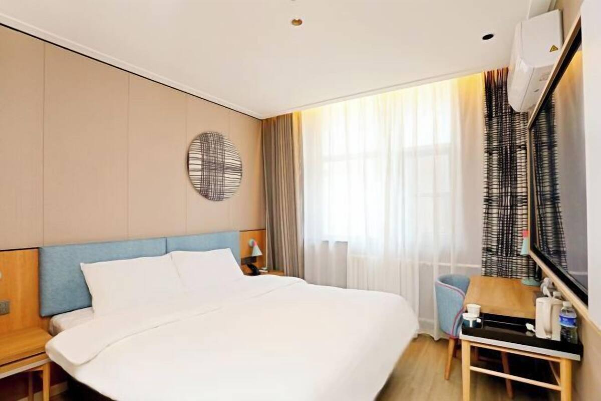A hotel room with a bed, a desk, a chair, a mirror, and a window with curtains.
