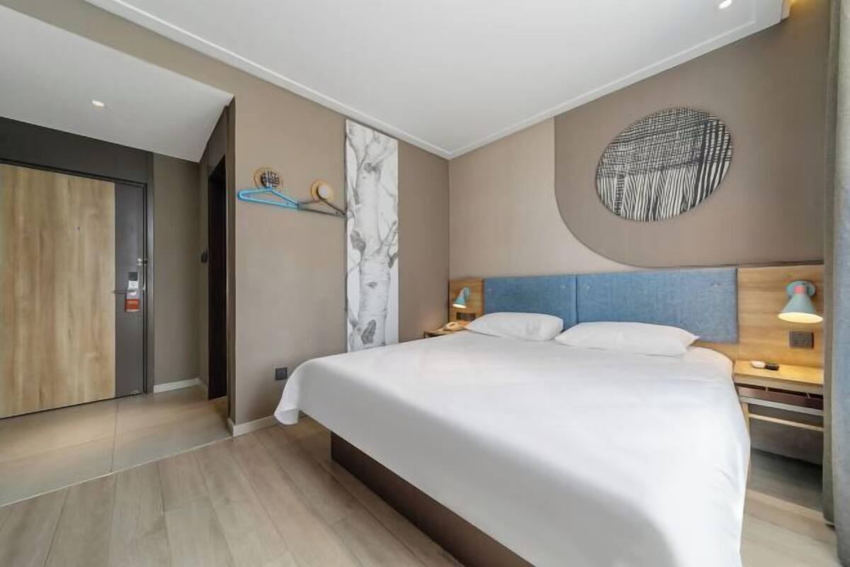A modern hotel room with a large bed, bedside tables, a wall-mounted artwork, and a door.