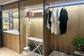 Habitació amb interior de fusta, una taula de planxar blanca i un penjador amb diverses peces de roba.