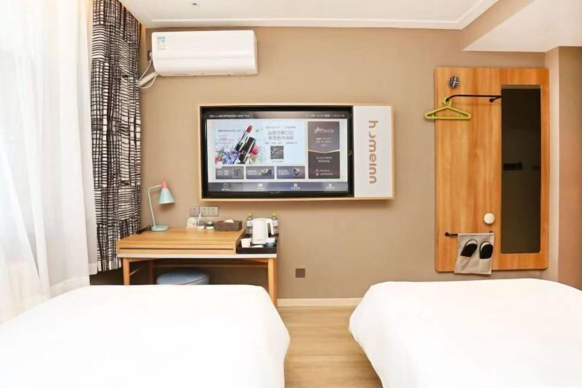 A hotel room with two beds, a desk with a computer, a TV, and a wooden door with a towel rack.