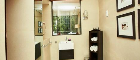 Une salle de bain moderne avec un grand miroir, un lavabo et un espace douche. Des tableaux encadrés ornent le mur, et un panier en osier est posé à proximité.