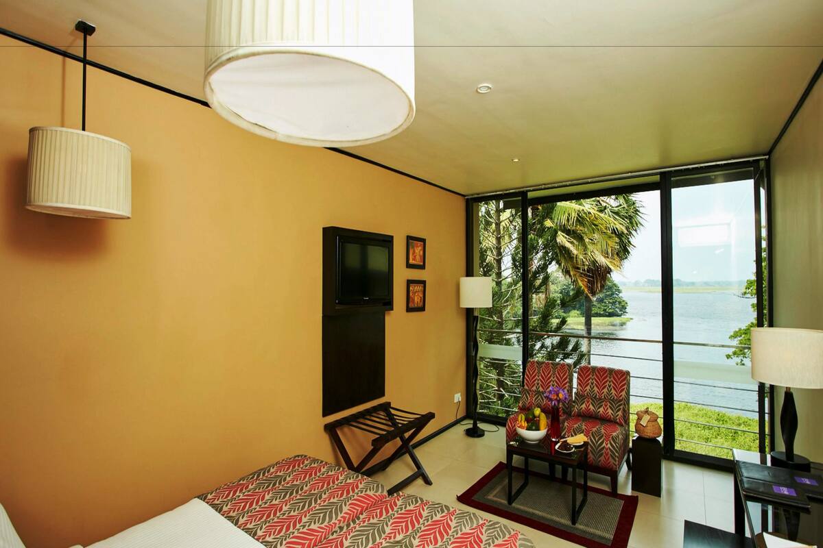 A modern hotel room with a bed, a TV, a sofa, and a view of a body of water.