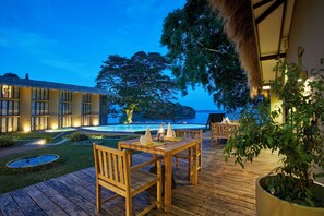 Une terrasse en bois avec une table et des chaises, un pot de fleurs et une vue sur un bâtiment et l’eau.