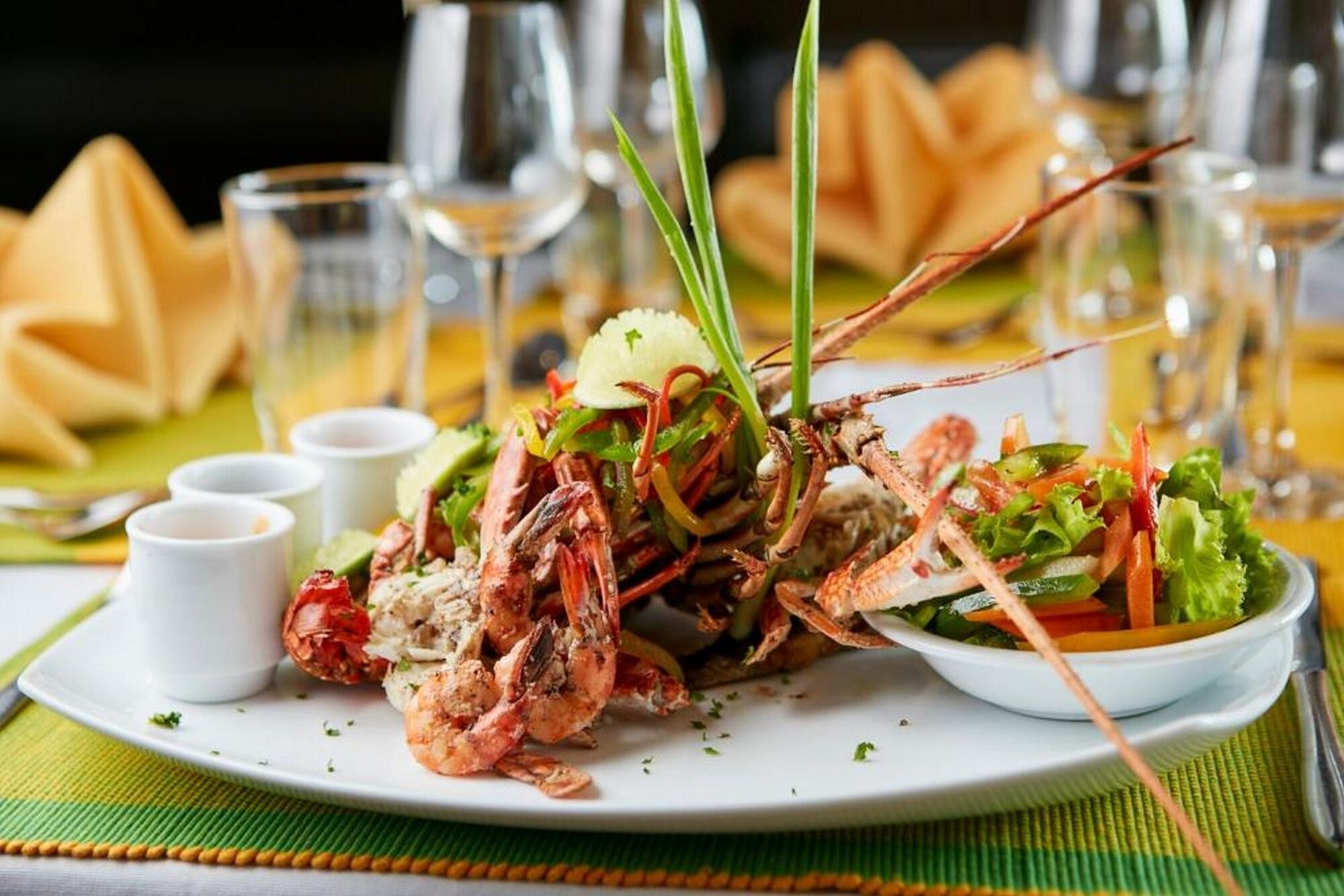 Plato de mariscos con cola de langosta y camarones, acompañado de ensalada y salsas para mojar.