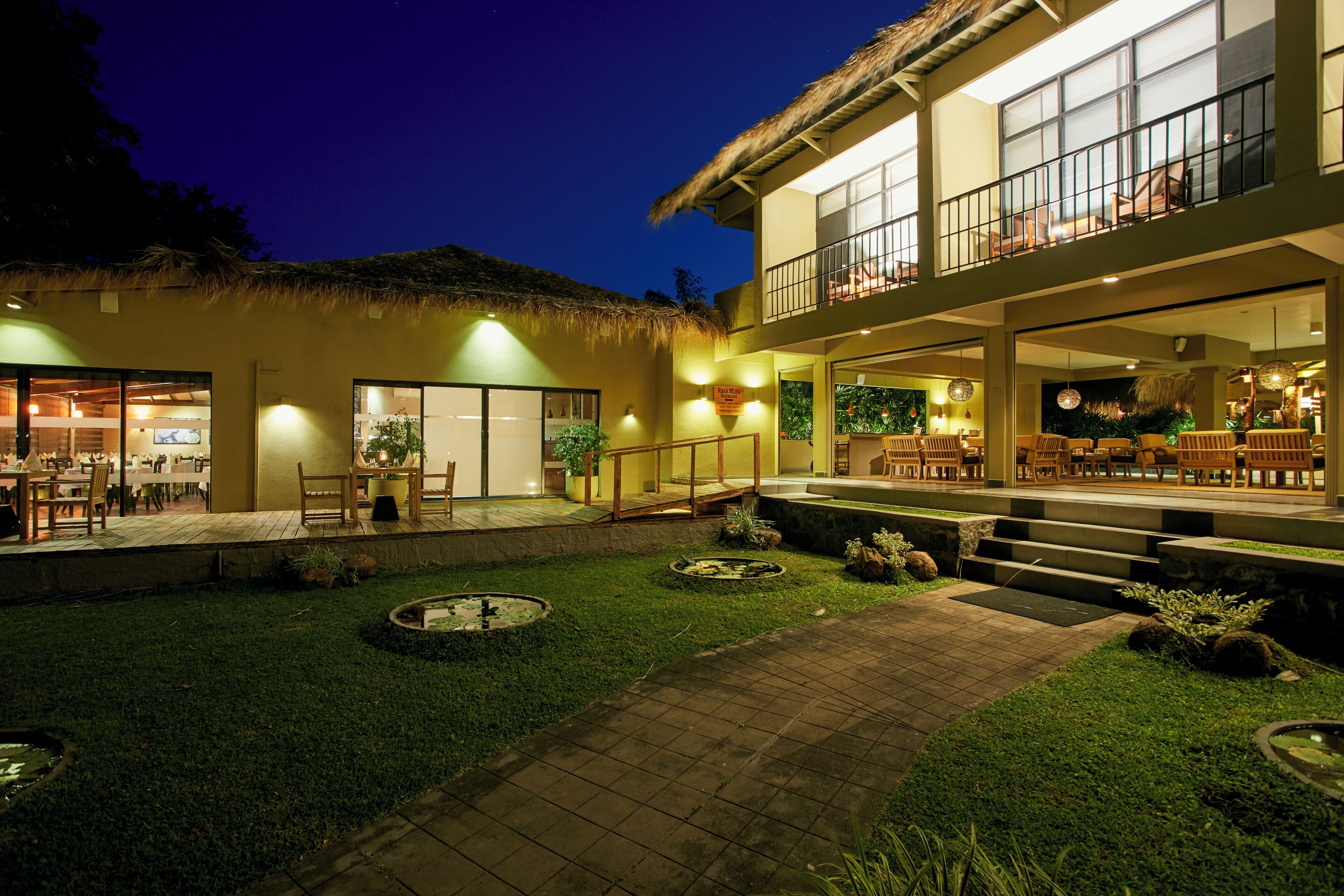 Un hotel con techo de paja, zona de estar al aire libre y jardín bien iluminado.