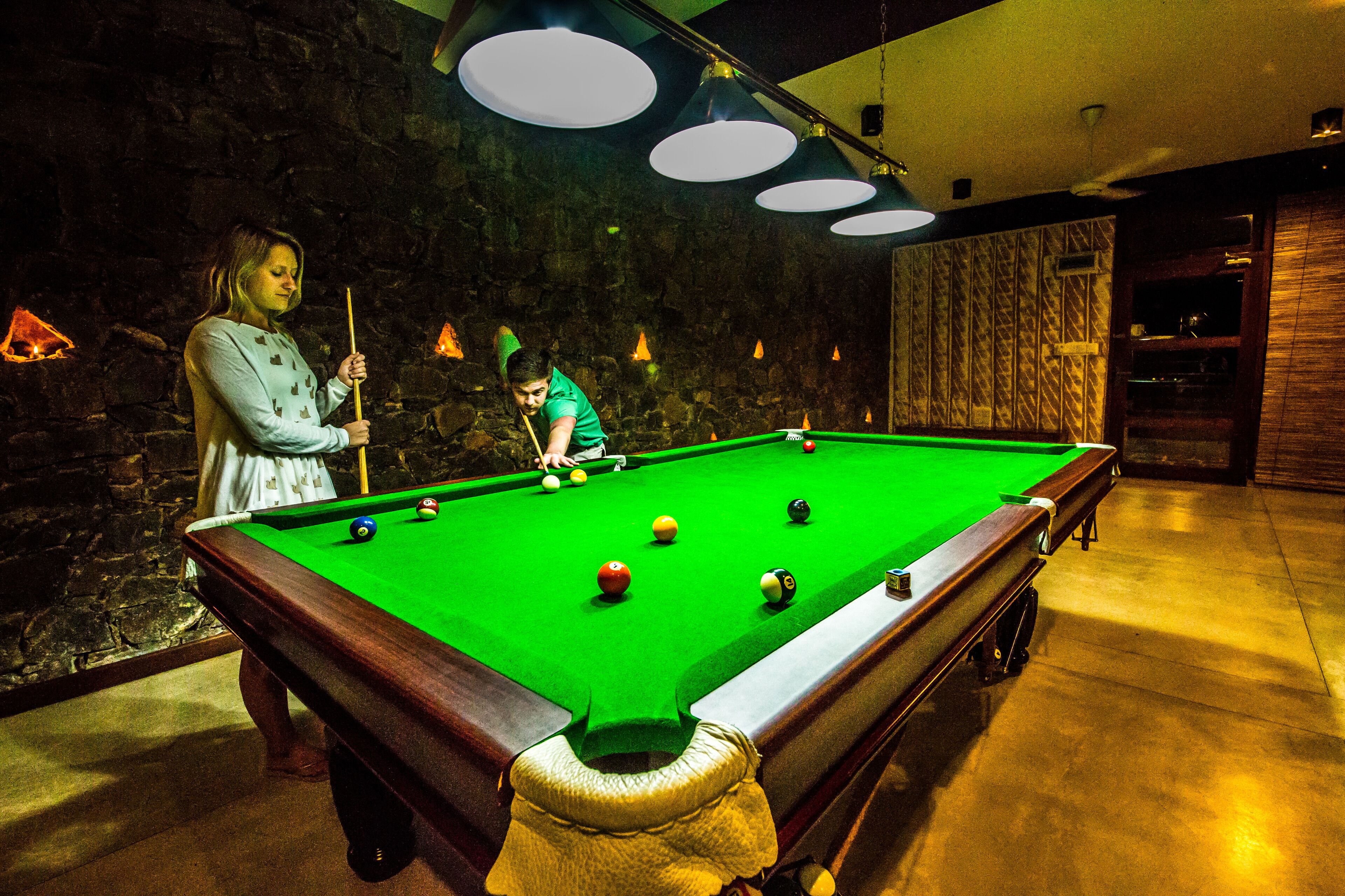 A pool table with balls, a person in a green shirt, and another person in a light blue shirt.