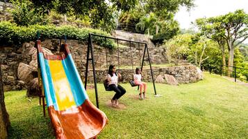 Playful fun awaits in this serene playground surrounded by lush greenery and a stone wall.