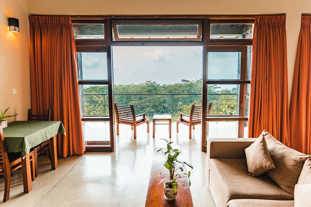 A room with a balcony, a dining table with chairs, a sofa, and a potted plant.
