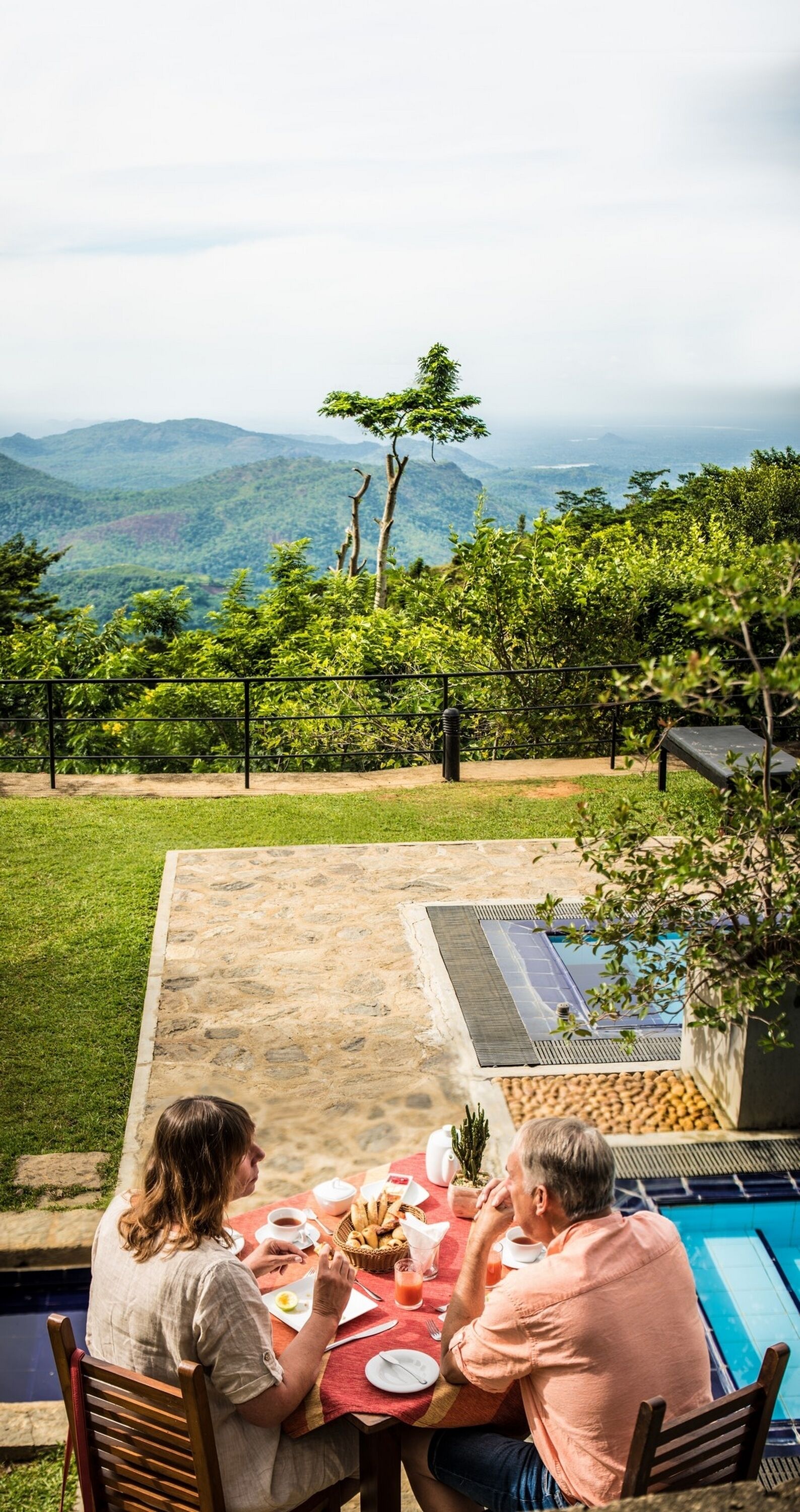 Ein Esstisch mit zwei Personen, Blick auf einen Pool und eine Berglandschaft.