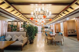 A spacious hotel lobby with a chandelier, sofas, dining area, and potted plants.