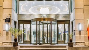 A revolving door entrance with a glass enclosure, potted plants on either side, and a stone wall backdrop. - Yuanfeng Hebei Hotel (Lhasa)