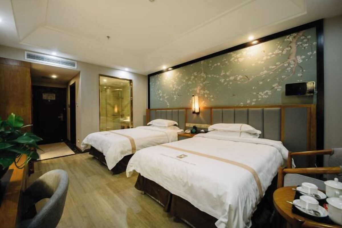 A hotel room with two beds, a desk, a chair, and a small table with cups and a tray.