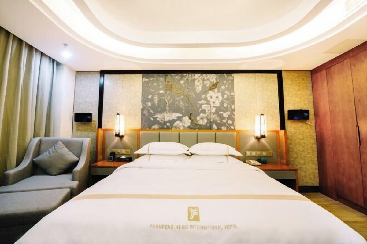 A hotel room with a large bed, two bedside tables, a chair, and a decorative wall panel.