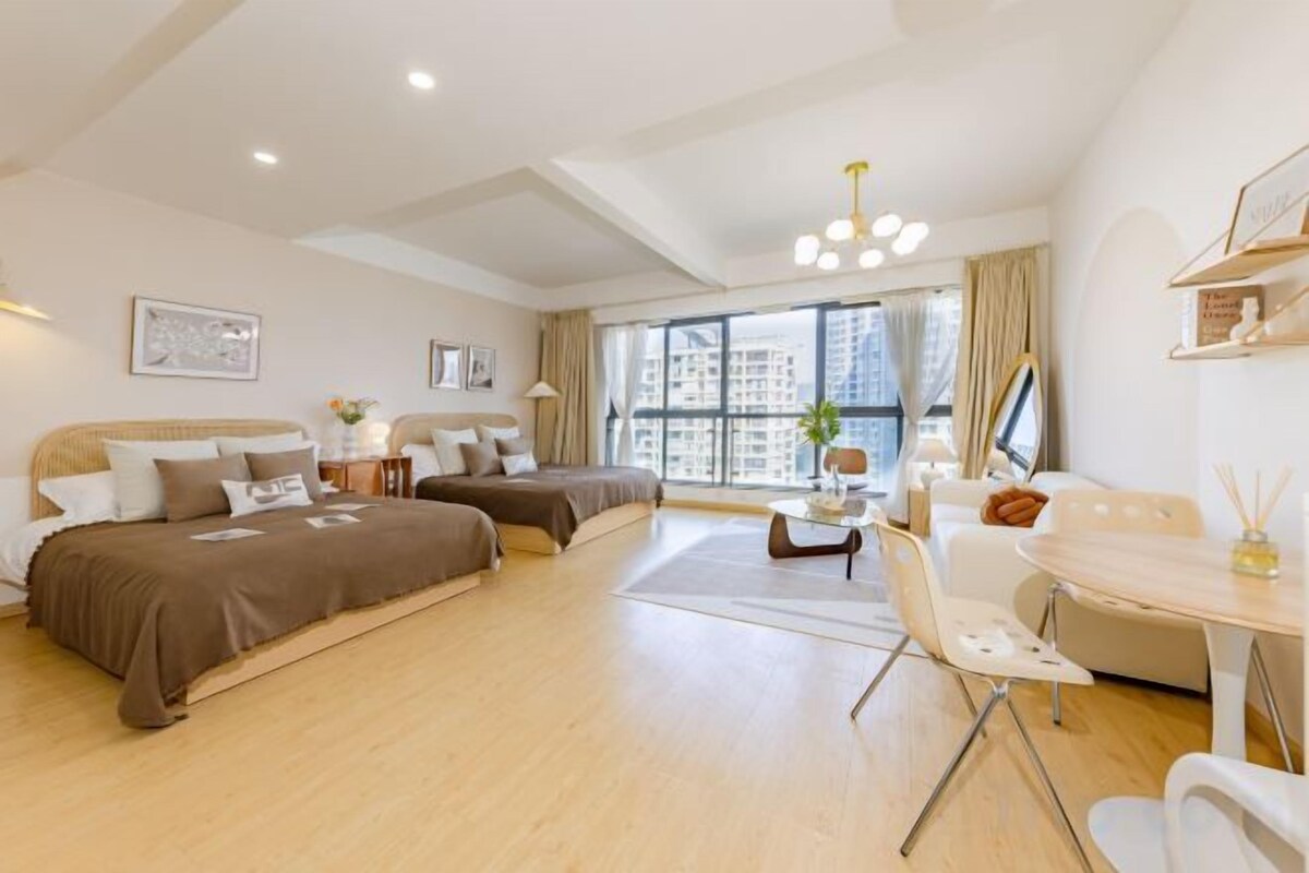 A hotel room with two beds, a dining area, and large windows.