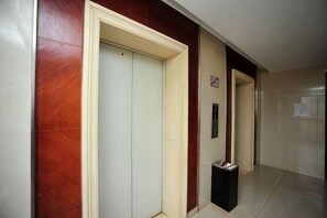 A hallway with a closed elevator door, a trash bin, and a door with a sign. - Kaili Internationa Hotel (Kunming)