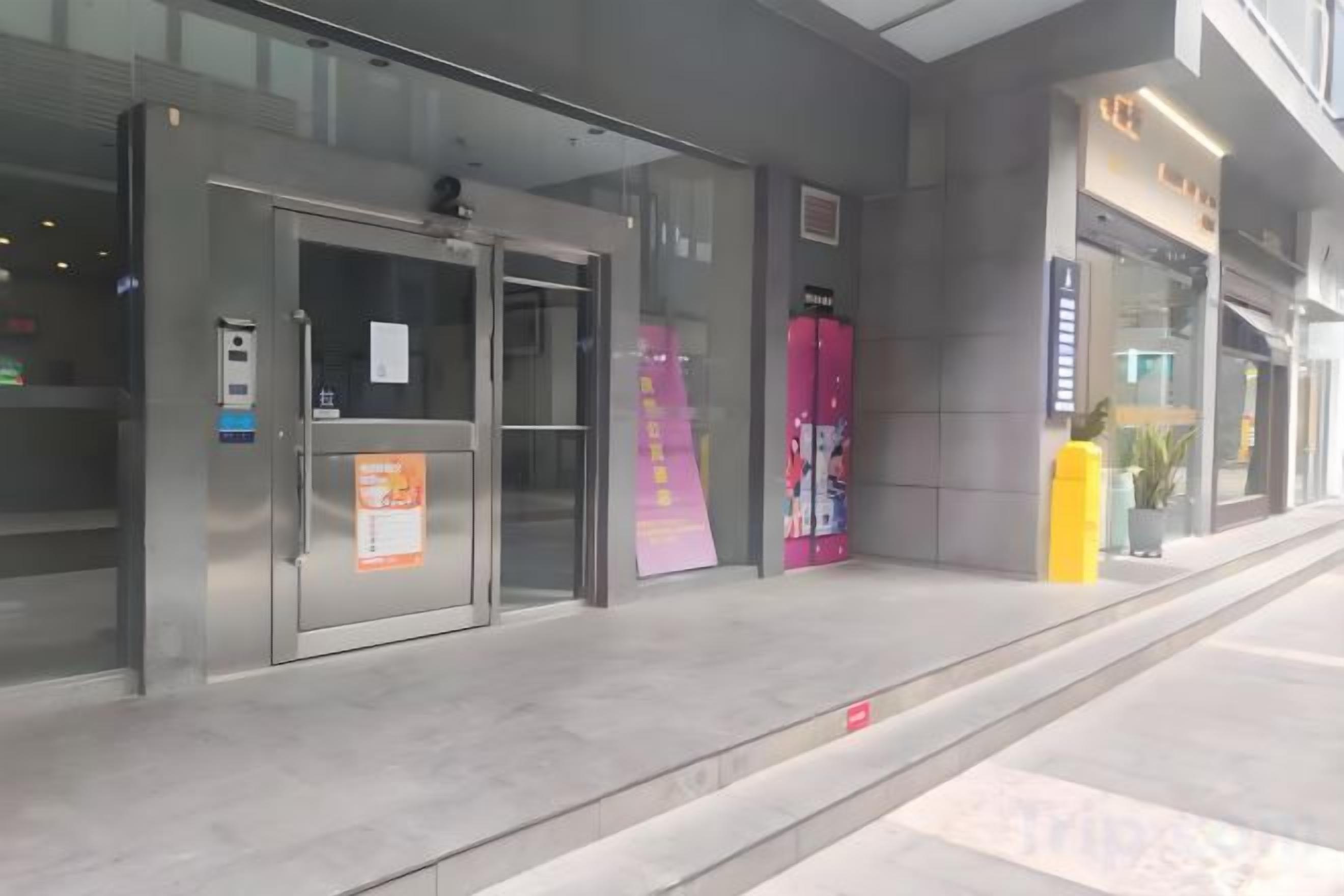 A hotel entrance with a glass door, a digital display, and a yellow pillar.
