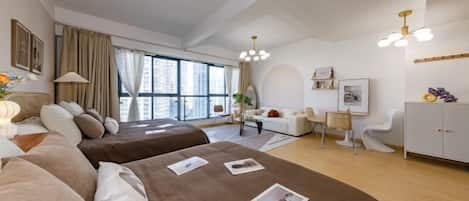 Una habitación de hotel moderna con dos camas, un área de descanso con sofá y sillones, un escritorio y un amplio ventanal con vistas a la ciudad.