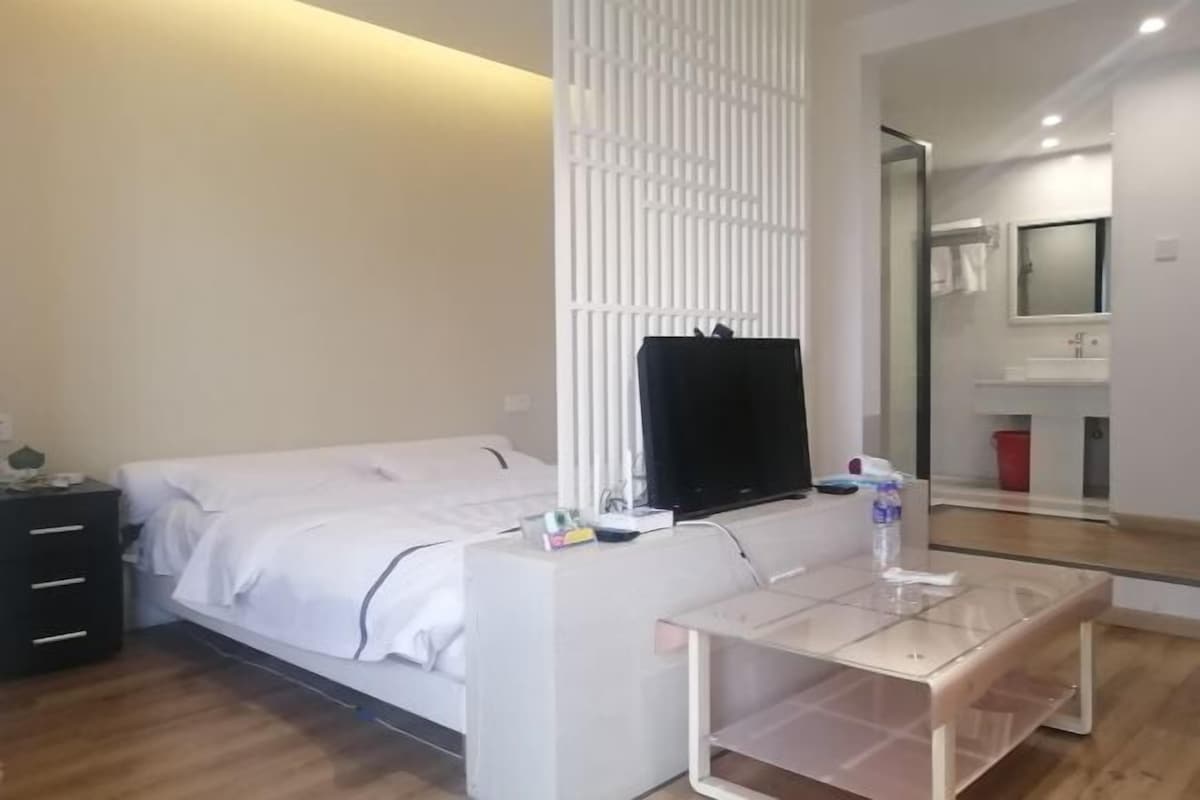 Quarto de hotel moderno com cama, televisão, mesinha e espelho.