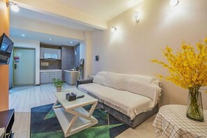 A modern living room with a sofa, a coffee table, and a dining table. There is a kitchen in the background with cabinets and a microwave. - Kaili Internationa Hotel (Kunming)