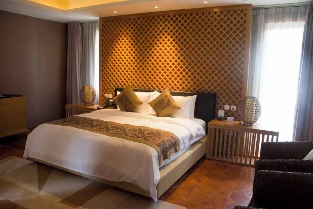 A hotel room with a large bed, a wooden headboard, a patterned wall, and a nightstand with a lamp.