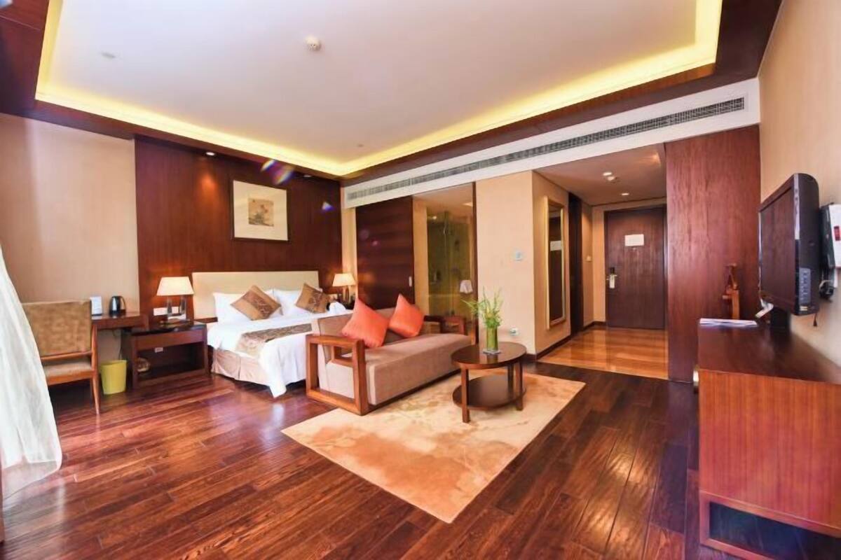 A hotel room with a bed, sofa, bedside tables, a TV, and a desk.