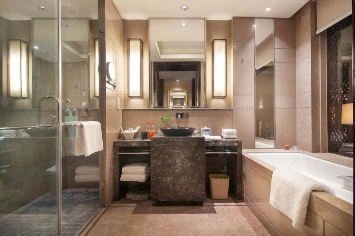 A modern bathroom with a glass-enclosed shower, a large mirror, a bathtub, and a vanity with a sink and towel storage.