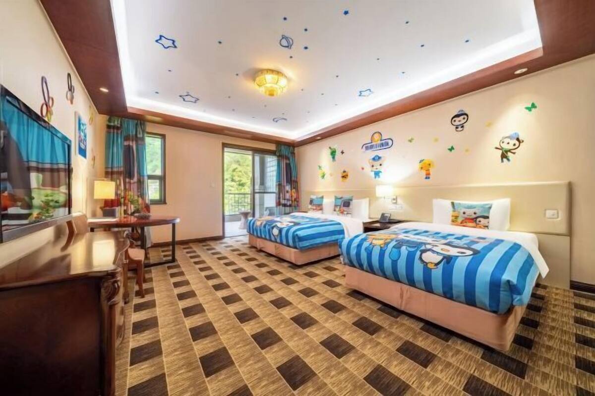 A hotel room with two beds, a desk, and a window.