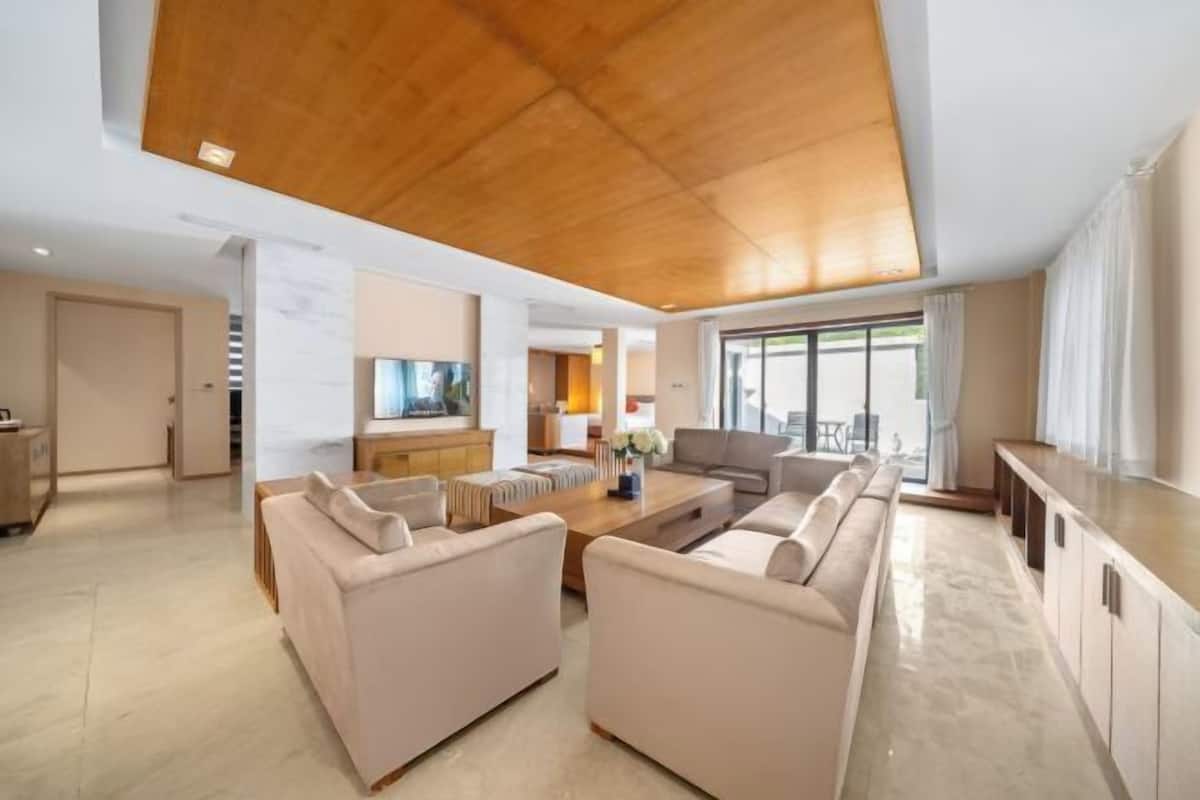 A spacious living area with a wooden ceiling, a kitchen in the background, and a large window providing natural light.