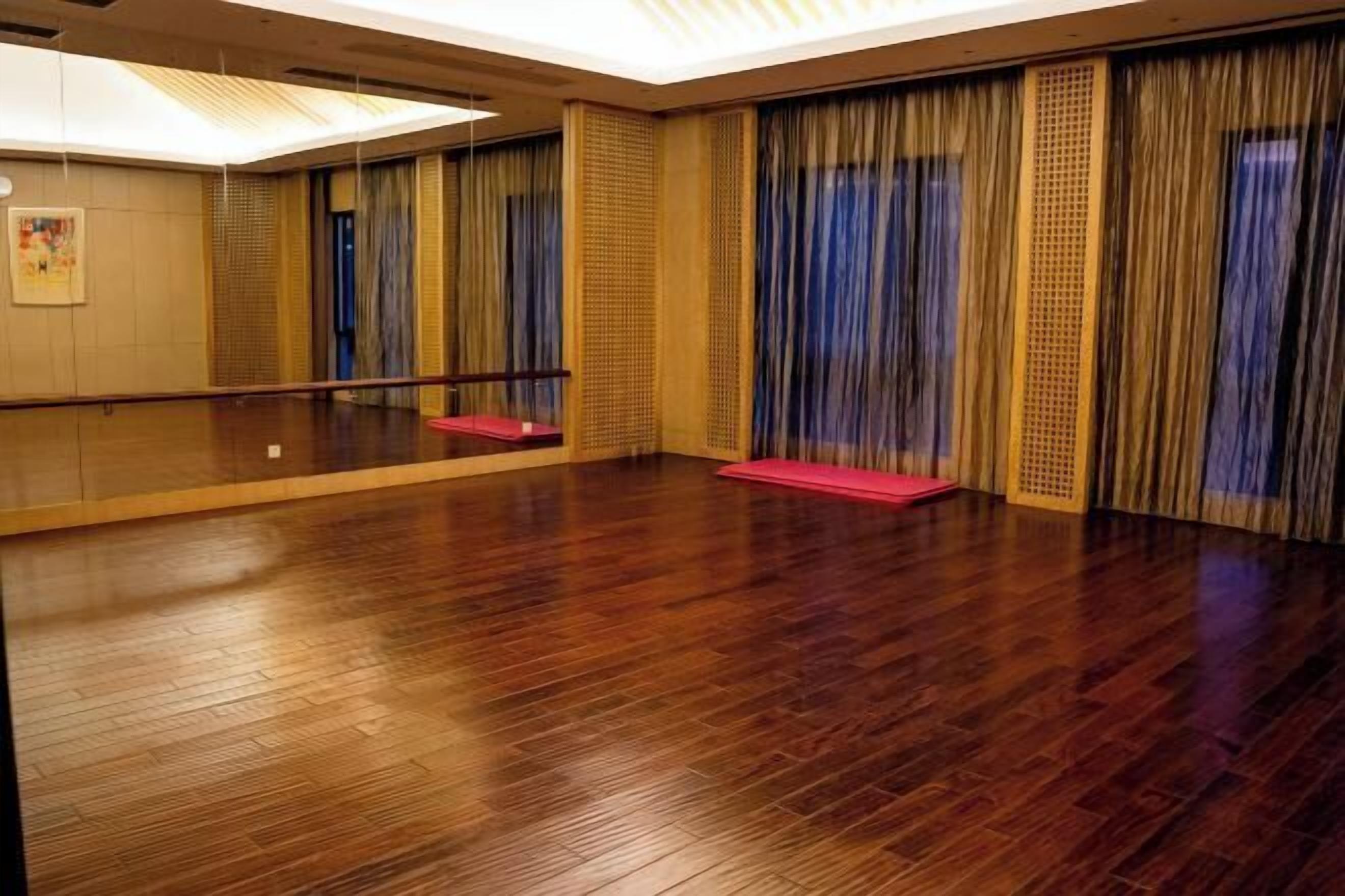 A spacious room with a wooden floor, a large mirror, and a red mat.