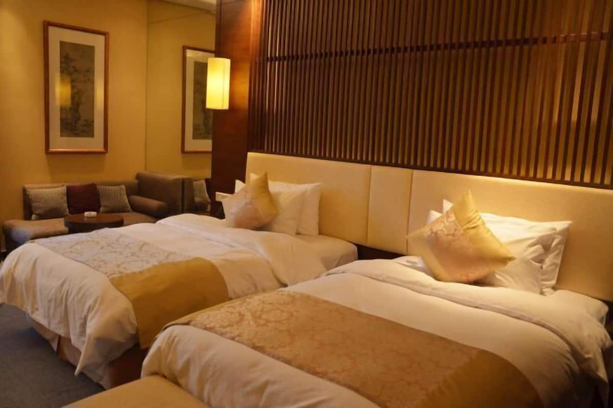 A hotel room with two beds, a sofa, and a wooden headboard.