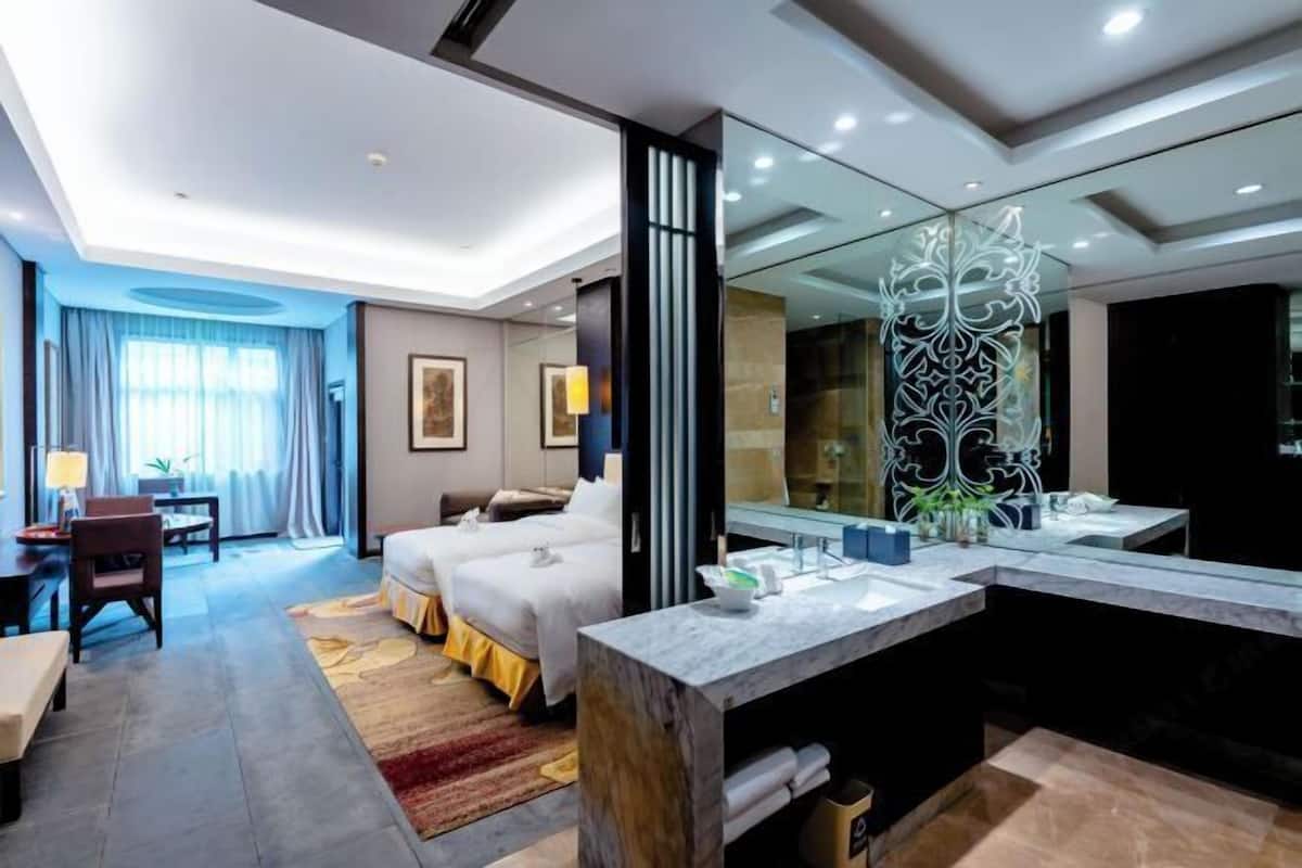 A hotel room with two beds, a sitting area with a table and chairs, a large mirror, and a modern bathroom with a vanity and sink.
