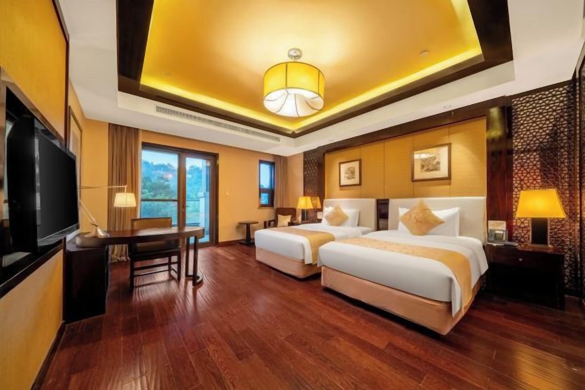 A hotel room with two beds, a TV, a desk, and a view of the outdoors.