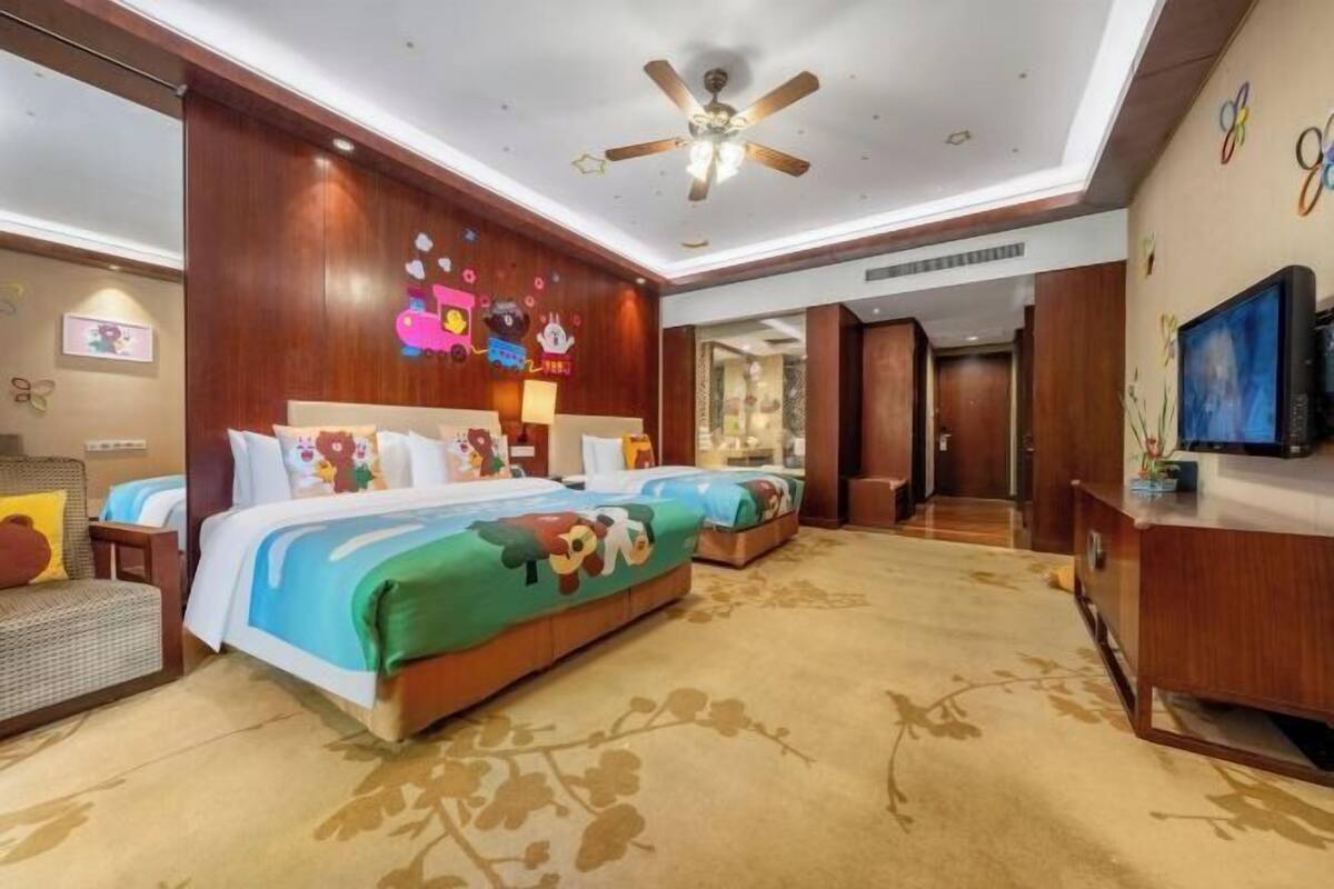 A hotel room with two beds, a ceiling fan, a TV, and a wooden wall with colorful decorations.