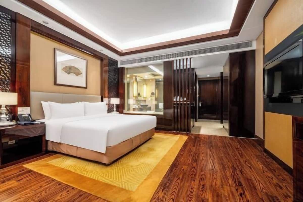 A hotel room with a bed, a desk, a TV, and a wooden floor.