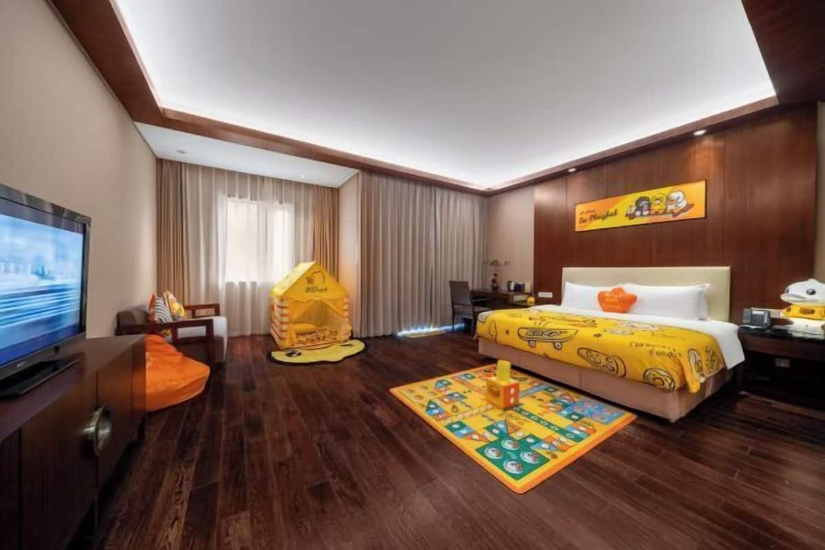 A hotel room with a bed, a TV, a play tent, and a children's play mat.