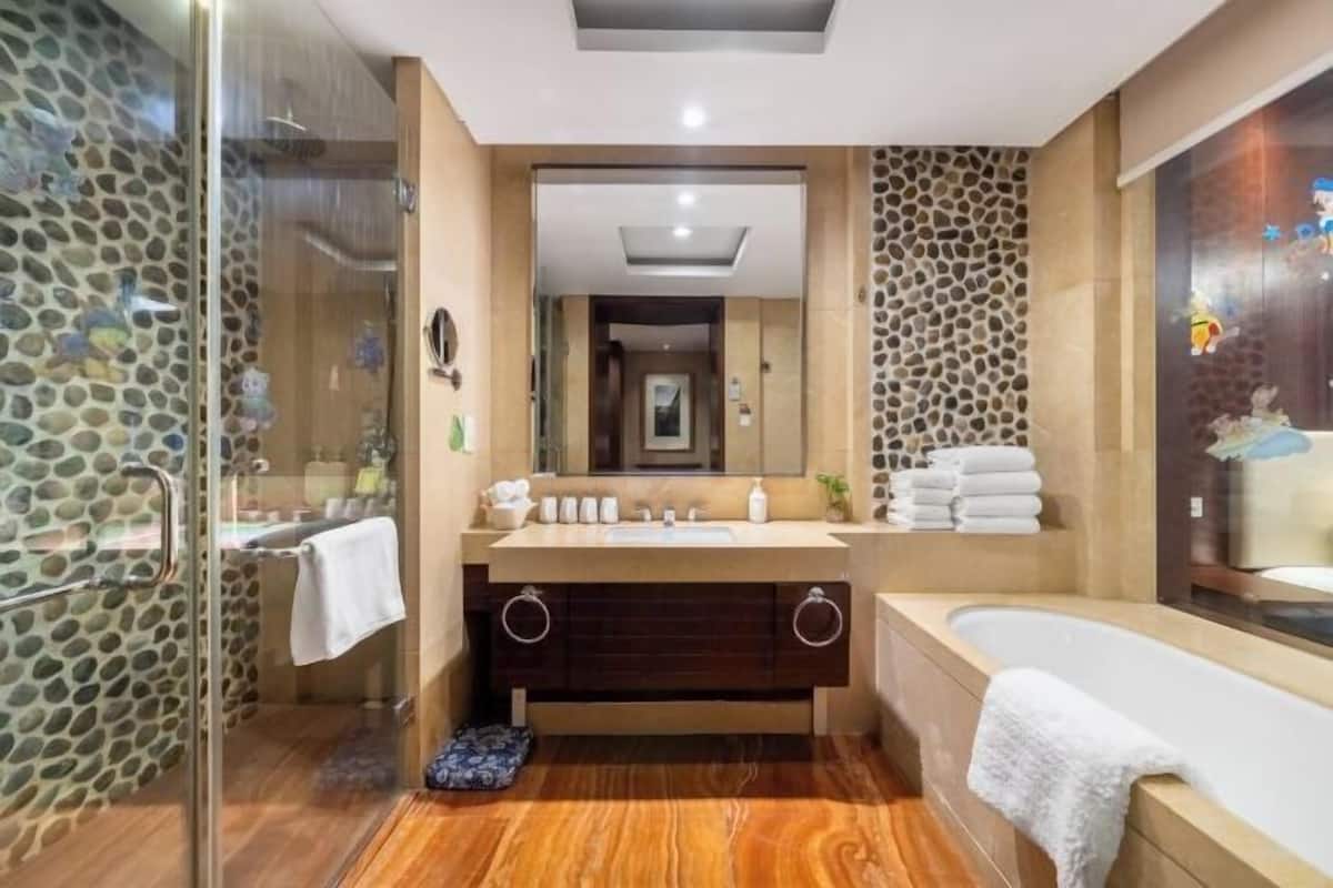 A modern bathroom with a glass shower, a bathtub, a vanity with a mirror, and a stone-patterned wall.