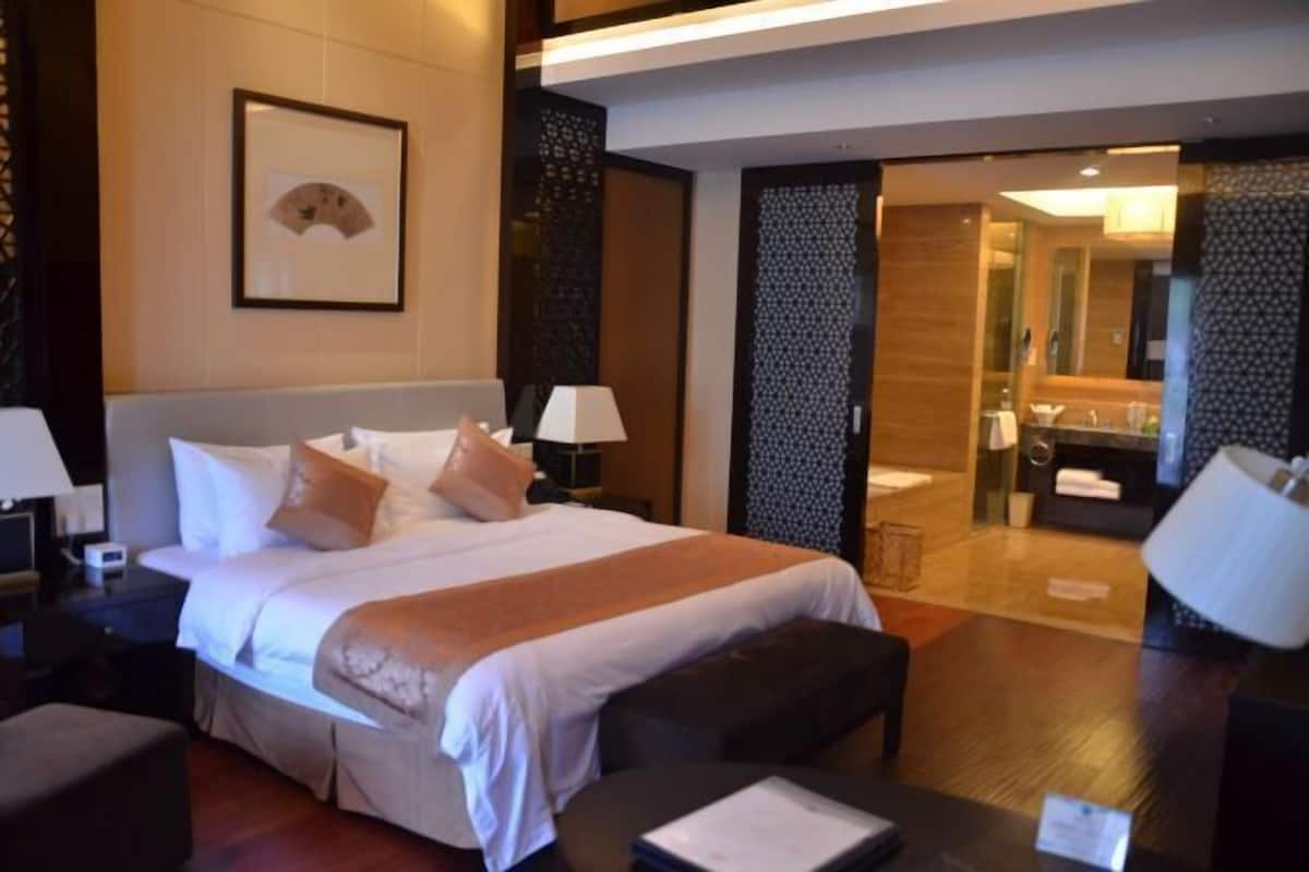 A modern hotel room with a large bed, bedside tables, a desk, and a bathroom visible through an open door.