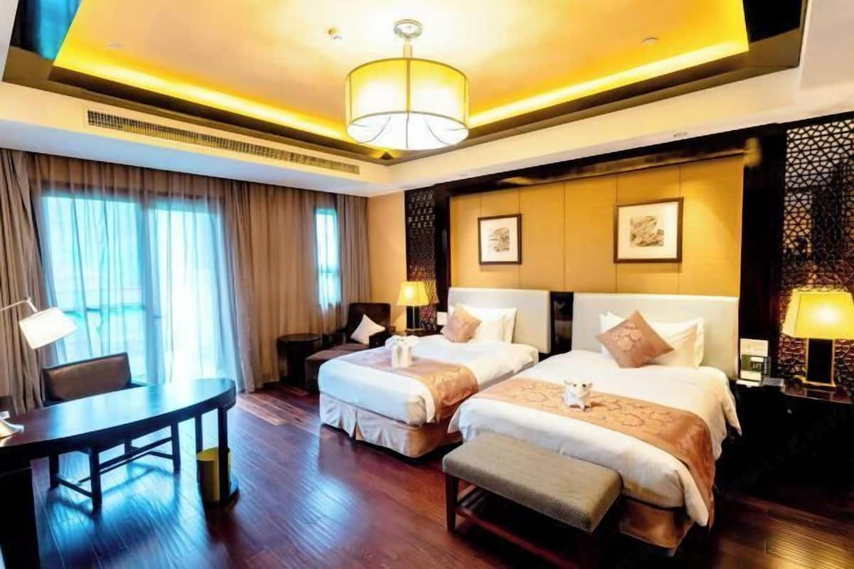 A hotel room with two beds, a desk, and a large window.