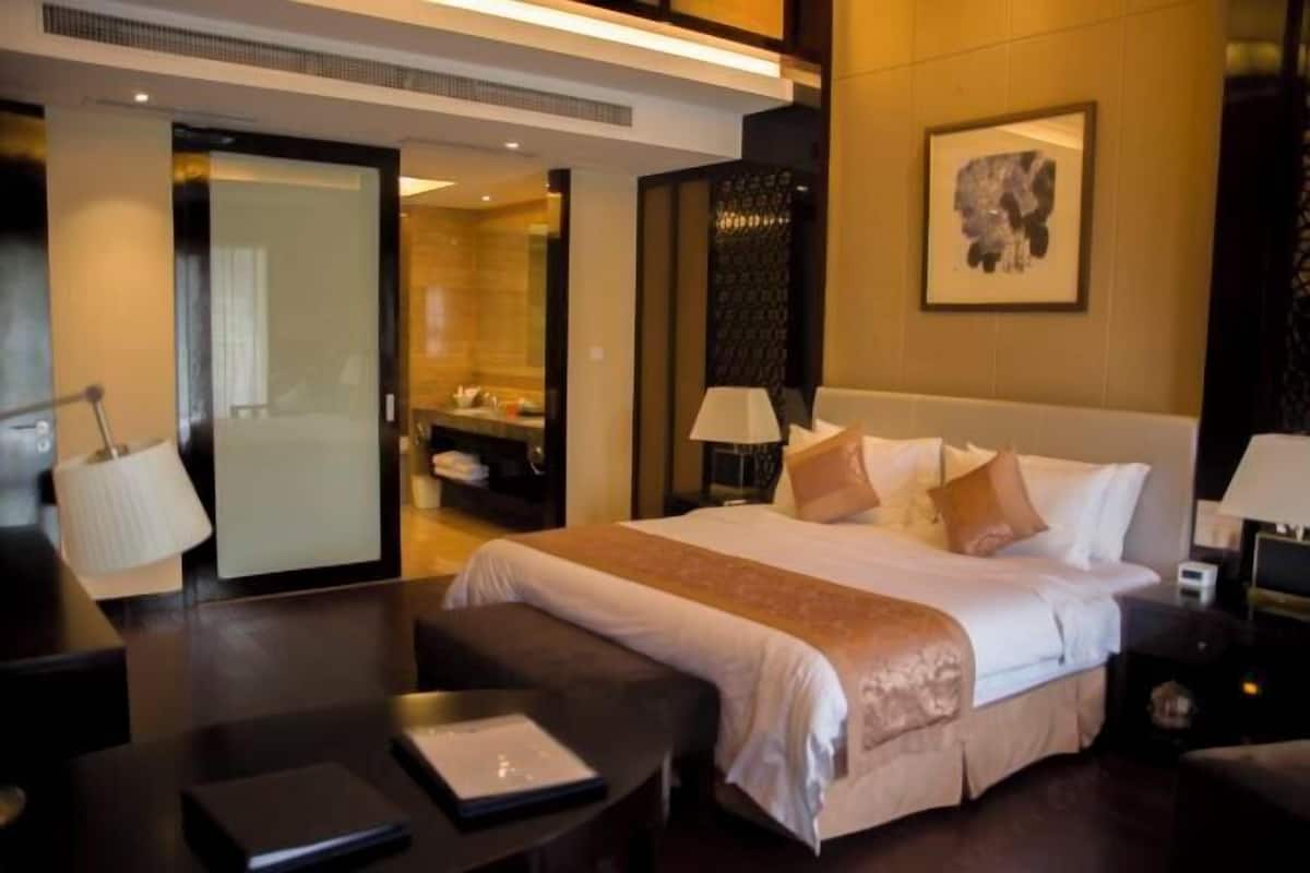 A hotel room with a large bed, bedside tables, a desk, a chair, a wardrobe, and a bathroom visible through an open door.