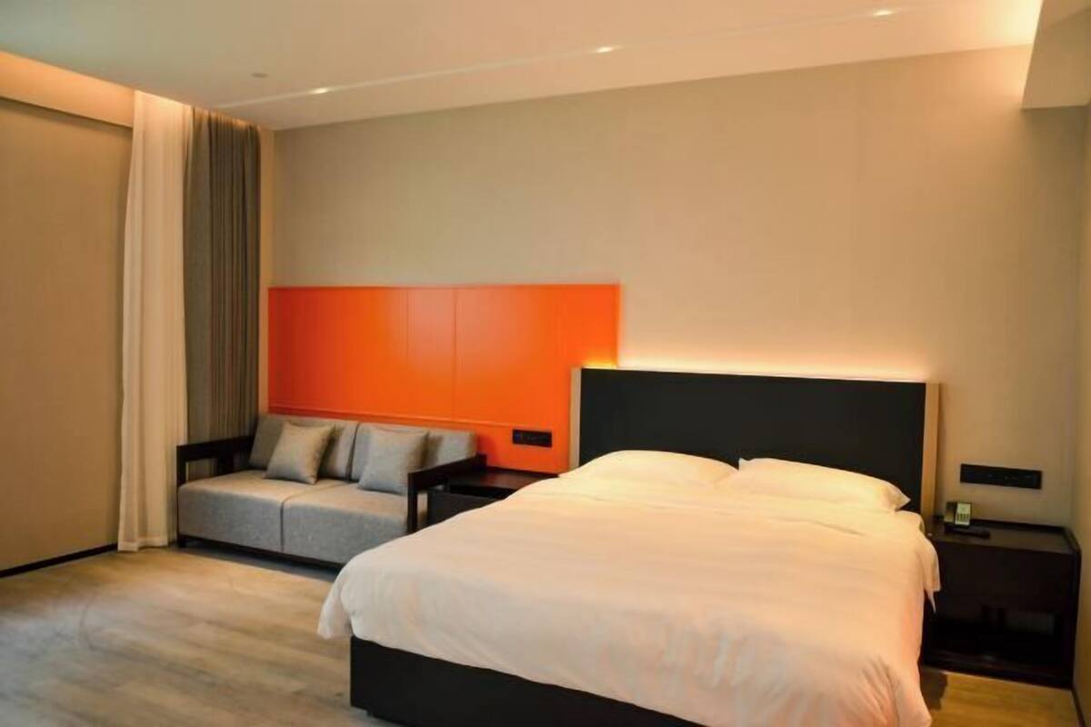 A modern hotel room with a large bed, a sofa, and a nightstand.